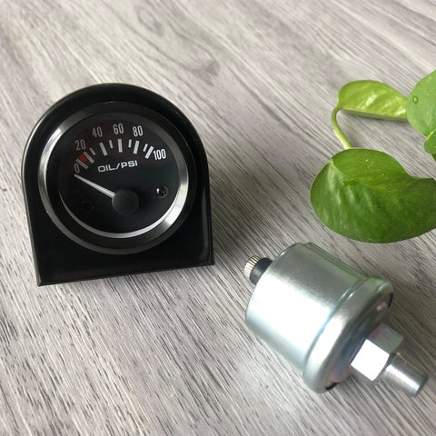 Front view of a 52mm oil pressure gauge with sensor and mounting hardware, black dial, 0–100 PSI.