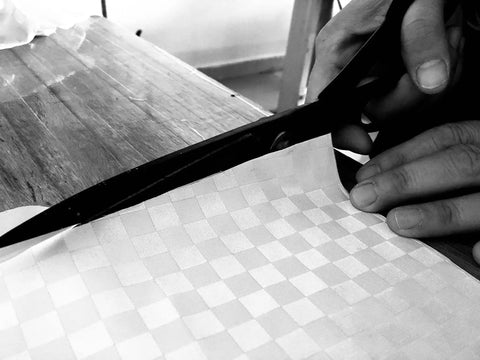 Close-up of hands cutting a checkered cloth material, suitable for Universal Piano Keyboard Dust Cover For 61 To 88 Keys Lightweight Adjustable.