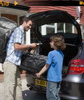 Man and child loading Beefy Heavy Duty Moving Bags Extra Large Storage Totes With Backpack Straps into car trunk, outdoor scene.