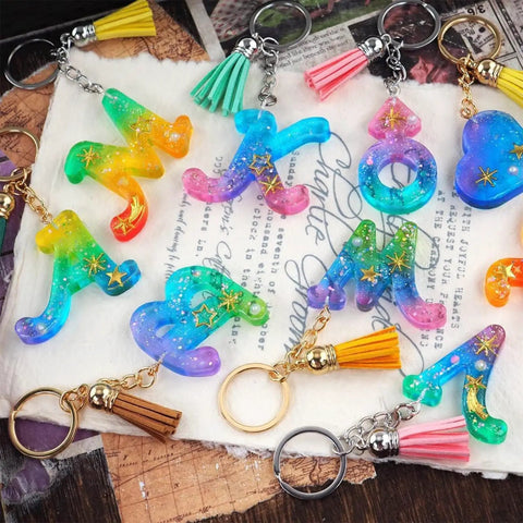 Colorful resin keychains shaped as letters with tassels, part of the 233 Piece Craft Toolkit Featuring Electric Hand Drill And Precision Bits For Resin Art And Keychain Making Includes Flat Nose Pliers Jump Rings And Screw Eyes Total Game Changer For Knocking Out Dope Jewelry.