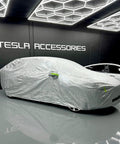Badass Heavy Duty Weatherproof Car Cover For Tesla Model X Silver Microfiber Weave fitted snugly over the vehicle in a showroom.