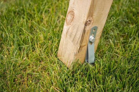 Wood post secured with Playset Anchor Kit For Swing Sets Heavy Duty Ground Anchors in grass, showing attached steel anchor and screw