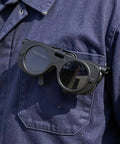 Premium Heavy Duty Industrial Double Lens Welding Goggles resting on a work uniform pocket, featuring dark lenses for glare reduction.