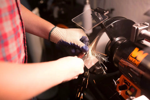 Person sharpening a metal blade using Rock Hard Bench Grinder with Eight Inch Grinding Wheels and a variable speed motor.