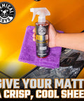 Hand holding Meticulous Matte Detailer And Spray Sealant For Crisp Satin And Matte Finishes Safe For OEM Vinyl 32 Fl Oz bottle on purple cloth