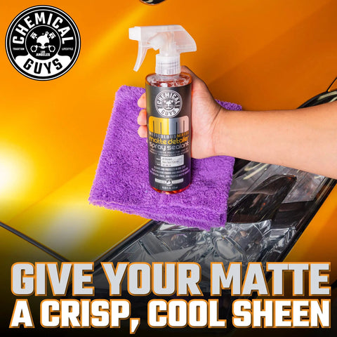 Hand holding Meticulous Matte Detailer And Spray Sealant For Crisp Satin And Matte Finishes Safe For OEM Vinyl 32 Fl Oz bottle on purple cloth