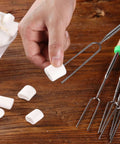 Hand holding marshmallow over telescoping stainless steel roasting sticks 32 inch 5 pack marshmallow skewers with wood handles for s'mores.