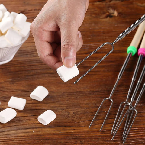 Hand holding marshmallow over telescoping stainless steel roasting sticks 32 inch 5 pack marshmallow skewers with wood handles for s'mores.