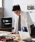 Office setting with man using a laptop, WorkForce Pro WF 4830 Wireless All In One Printer visible on desk, showing touchscreen.