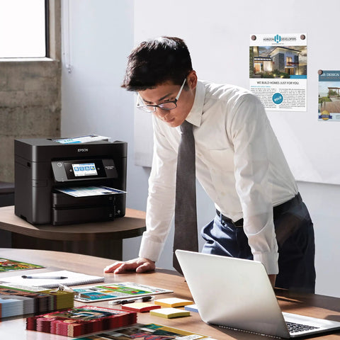 Office setting with man using a laptop, WorkForce Pro WF 4830 Wireless All In One Printer visible on desk, showing touchscreen.