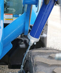 Blue lever-action grease gun with metal extension and hose near a rugged tire on heavy machinery