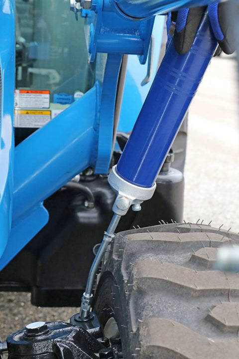 Blue lever-action grease gun with metal extension and hose near a rugged tire on heavy machinery