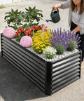 Raised Garden Bed Kit 6x3x1 Ft Metal Planter Boxes Outdoor With No Fuss Easy Assembly For Vegetables Fruits Flowers And Herbs Large Rectangle Garden Bed In Dark Gray Durable Galvanized Steel Construction, installed with plants and person watering.