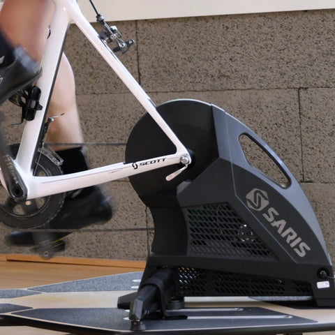 Indoor cycling setup featuring a quick release bike trainer skewer for rear wheel replacement, showing silver finish and alloy material.