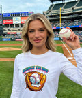 Woman in a white long-sleeve shirt with 'Respect the Drip' ice cream drip baseball patch at a stadium, holding a baseball.