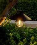 Lit solar metal lantern hanging from tree branch, part of 2 Pack Solar Metal Hanging Lanterns With Shepherd Hooks For Outdoor LED Garden Lighting Black Pathway Porch Yard Decor That Pops Durable Weatherproof Landscape Lights