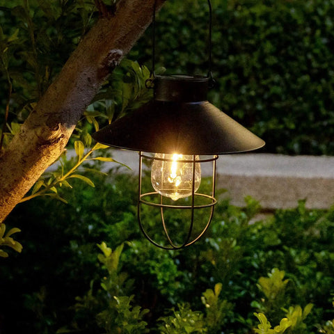 Lit solar metal lantern hanging from tree branch, part of 2 Pack Solar Metal Hanging Lanterns With Shepherd Hooks For Outdoor LED Garden Lighting Black Pathway Porch Yard Decor That Pops Durable Weatherproof Landscape Lights
