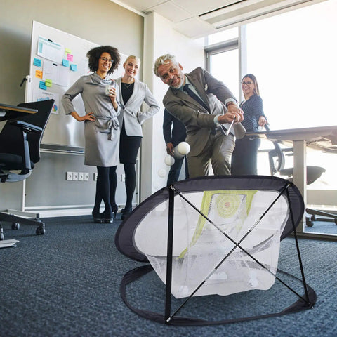 Golfer using Golf Chipping Net for Backyard Practice With Foldable Pop Up Frame indoors surrounded by colleagues.