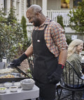 Man cooking on a griddle using the Griddle Essential 5 Piece Tool Set with spatula, scraper, and squeeze bottles, outdoor gathering