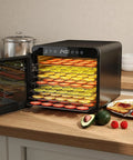 Top Tier Food Dehydrator With Seven Sturdy Stainless Steel Trays And No Sweat One To Twenty Four Hour Timer For Smooth Quiet Jerky Fruit Veggie Herb Treat Drying, showing trays filled with colorful slices on a kitchen counter.
