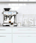 Oracle Fully Automatic Espresso Machine In Brushed Stainless Steel With 58 mm Portafilter on kitchen counter with coffee accessories.