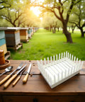Queen Marker Cage Clip for Beekeeping tool on table with beehives in background, white plastic design for easy handling.