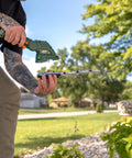 Person using Cordless Grass Shear And Shrub Trimmer With Wheeled Extension Handle Seven Point Two Volt Lithium Ion Battery.