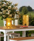 Outdoor scene with Cordless Battery Operated LED Glass Lamp With Timer Yellow Table Centerpiece, glowing on wooden table.