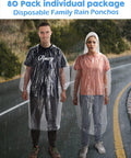Two adults wearing clear 80 pack disposable adult rain ponchos on road, hooded with elastic cuffs for theme parks and outdoor adventures.