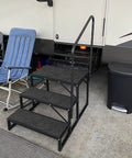 Heavy Duty Three Step RV Stair With Solid Handrail Steel Frame Rated For 600 LBS Load Capacity next to camping chair and trash can.
