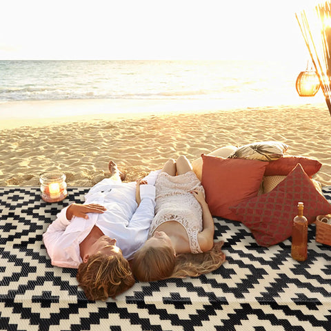 Couple relaxing on Waterproof Outdoor Rug 5x8 Ft Reversible Plastic Area Rug For Patio Deck Backyard RV Beach Camping Black And Beige Large Modern Floor Mat For All Weather Outdoor Use at beach