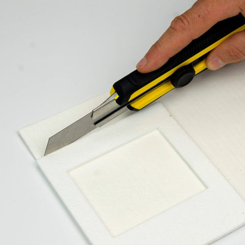 High-temperature gasket paper being cut with a yellow-black utility knife; white gasket sheet.