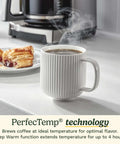 14 Cup PerfecTemp Programmable Coffee Maker With Glass Carafe And 1 4 Cup Setting Brew Strength Control Brew Pause And Over Ice Function In Black Stainless Steel on counter behind steaming mug and pastry