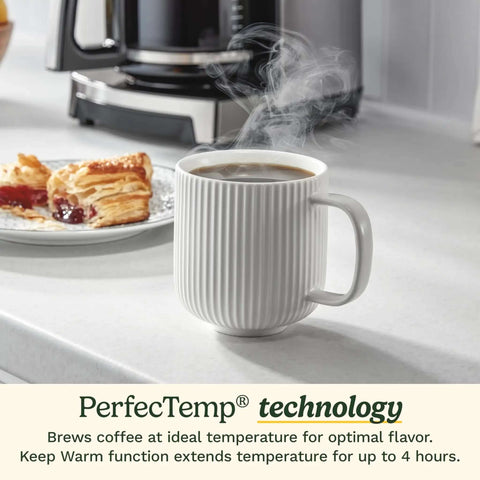 14 Cup PerfecTemp Programmable Coffee Maker With Glass Carafe And 1 4 Cup Setting Brew Strength Control Brew Pause And Over Ice Function In Black Stainless Steel on counter behind steaming mug and pastry