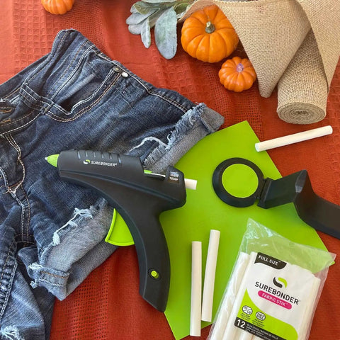 Cordless High Temperature Glue Gun 60W with standby base, glue sticks, and craft materials, including denim and burlap, on table