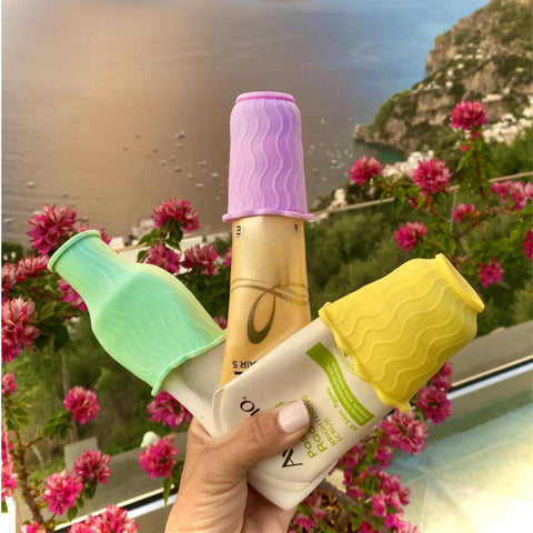 Elastic Toiletry Sleeve Set Keeps Liquids From Leaking In Luggage, Leak Proof Travel Bottle Covers For Standard And Travel Sized Toiletries, Reusable Accessory For Travel Bags And Carry On On The Go; hand holding colorful sleeves on bottles by flowers