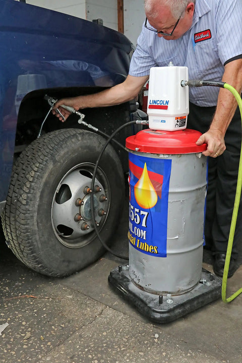 Mechanic using Lincoln 917 Pro Grade 50 To 1 Pneumatic Grease Pump, Heavy Duty Air Operated For 120 Lb Drums on vehicle wheel.