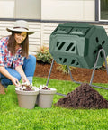 Woman using Outdoor 42 Gallon Dual Chamber Compost Tumbling Bin With 360 Degree Rotating Barrel on lawn with metal frame