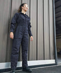 Heavy Duty Poly Cotton Twill Coverall In Dark Navy With Alpha Fit Snag Resistant Trims worn by a woman near a garage wall.