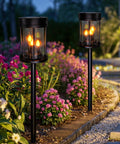 Outdoor Solar Stake Lights With Flickering Candle Lanterns For Yard And Patio 2 Pack Black Garden Pathway Lights next to flowers