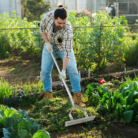 Man using 20 Inch Wide Lawn Dethatcher Rake With Long Handle, 19 Curved Tines, Adjustable From 25 To 60 Degrees in garden.
