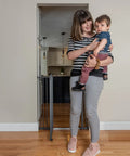 Woman holding child next to the Extra Tall Decor Safety Gate For Kids And Pets In Gray Fits Openings From 28 To 38.25 Inches Wide And 36 Inches High Perfect For Doorways Stairways And Between Rooms No Fuss Install With Extensions And Stair Kit in hallway.