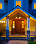 Front porch with 31.5 Inch Farmhouse Chandelier With Rustic Wagon Wheel Silhouette in Vintage Rust and Black Finish illuminated at night
