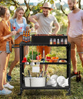 Four people enjoying outdoor cooking with Outdoor Grill Cart Table With Pizza Oven Stand For Indoor And Outdoor Cooking 4 Locking Casters Side Handle Hooks Spice Caddy Paper Towel Holder Large Prep Surface Heavy Duty Black in a garden setting.