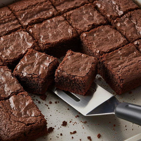 Close-up of mini stainless steel spatula beside brownie squares on a baking sheet.