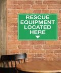 Rescue Equipment Located Here green sign on brick wall above chair and table in indoor setting.