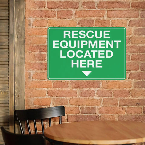 Rescue Equipment Located Here green sign on brick wall above chair and table in indoor setting.