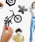 Hand applying Stranger Things Peel And Stick Wall Decals Set With 17 Pieces Removable And Repositionable Without Residue For Any Smooth Surface Perfect For Renters And Homeowners Seeking Retro Sci Fi Style And Easy Decor Makeover featuring retro sci-fi characters and symbols.