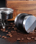 Top Shelf 58mm Espresso Distributor And Tamper Set beside coffee beans and ground coffee on a black surface.