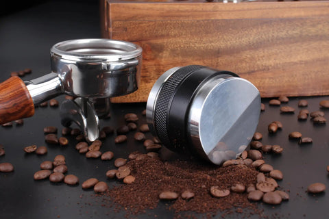 Top Shelf 58mm Espresso Distributor And Tamper Set beside coffee beans and ground coffee on a black surface.